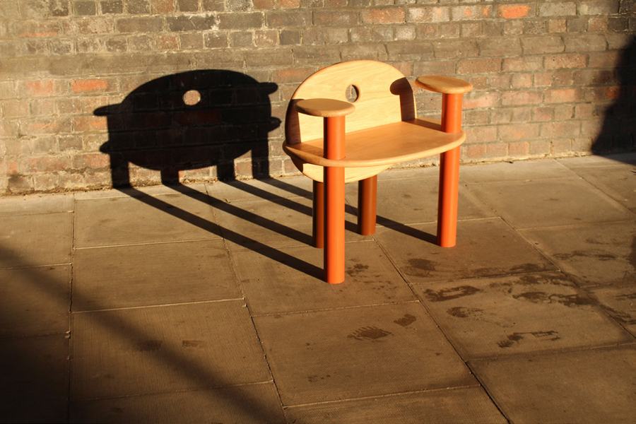 The TOT Chair from the front, its barrel-shaped shadow on brick