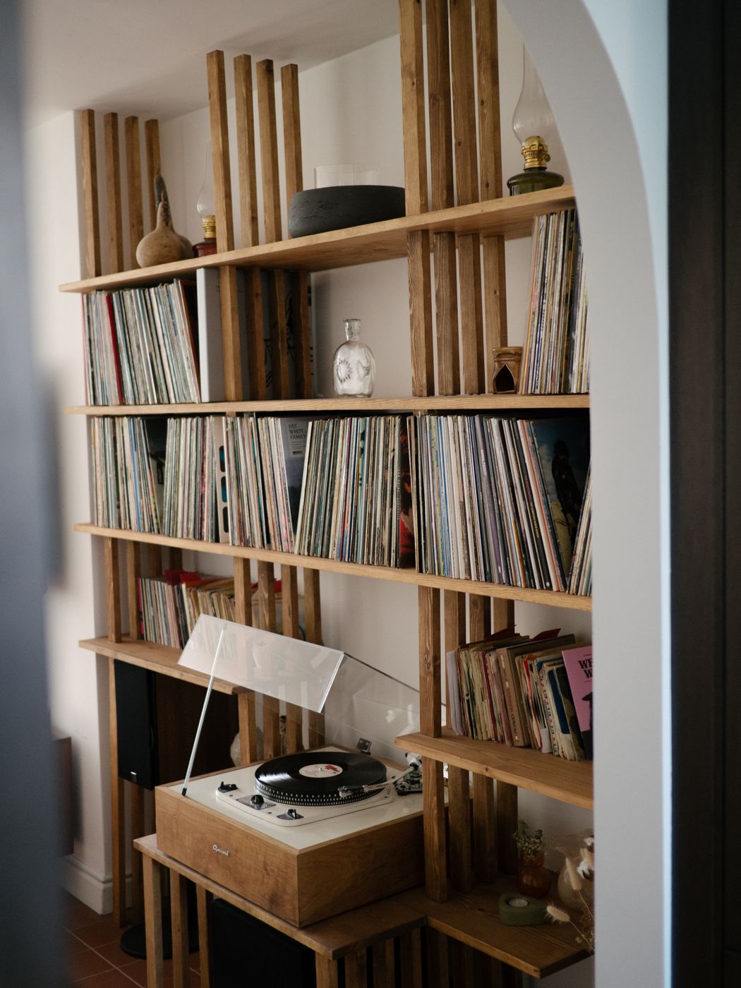 Bespoke shelving unit filled with records, a turntable on its slatted stand, seen through an arched doorway