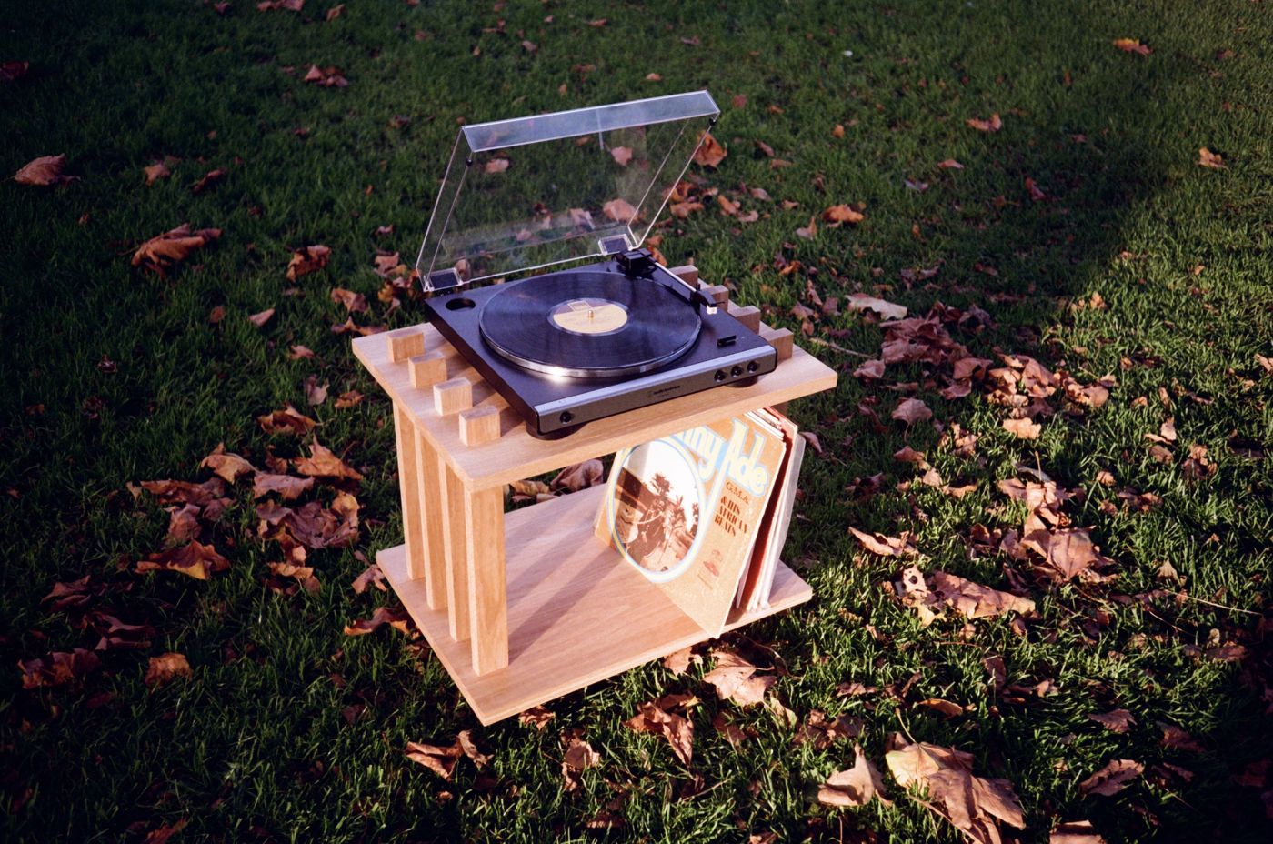 Turntable Table on autumn grass, a record spinning on top and LPs stored underneath