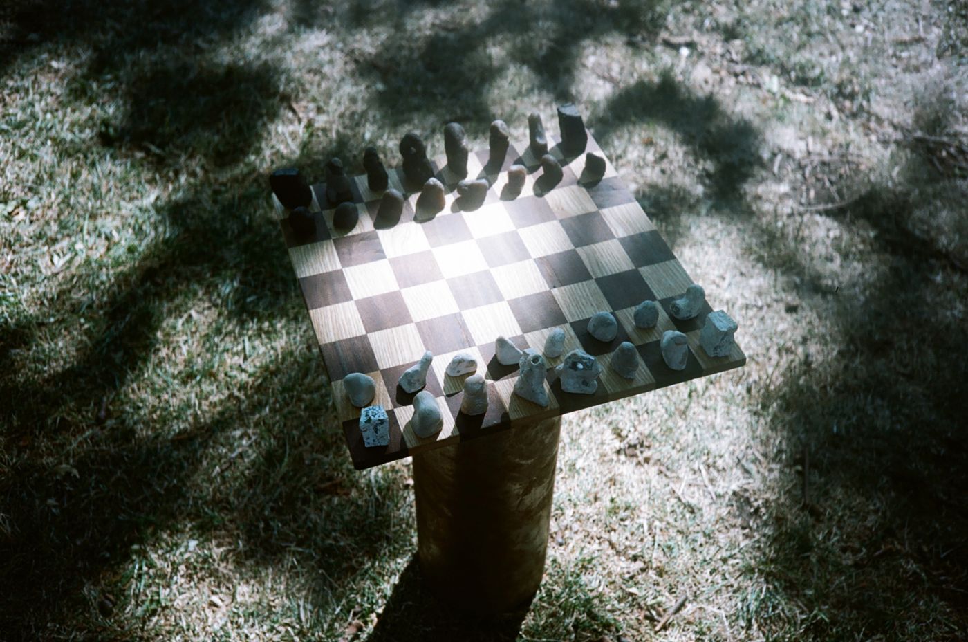 The chess set on a rusted column in dappled shade, seen from above